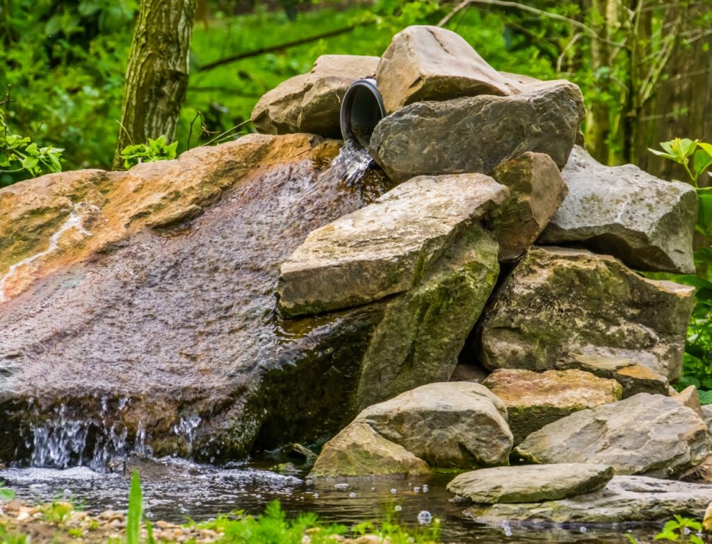 small waterfall made out of boulders in a garden, simple and beautiful garden architecture, pond decorations, nature background