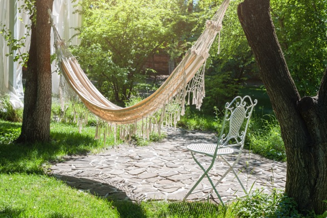 Summer garden with hanging hammock for relaxation. Lazy time, siesta. Beautiful landscape, sunny day