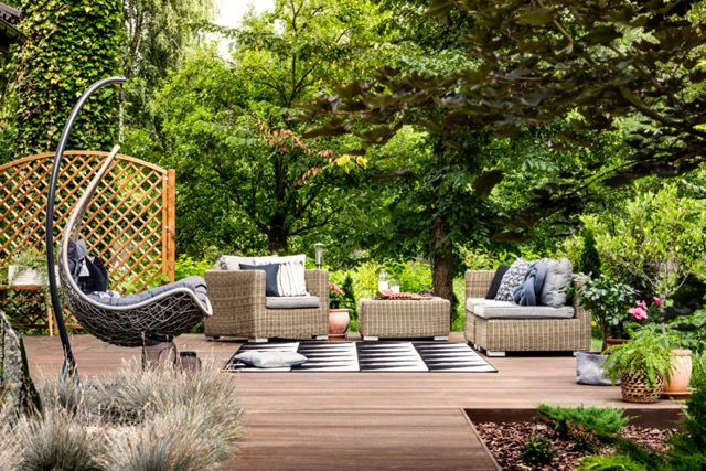 Hanging chair and geometric carpet on wooden patio with rattan garden furniture